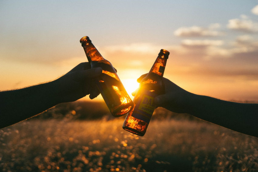 Image de 2 mains en train de trinquer avec des bières au soleil couchant